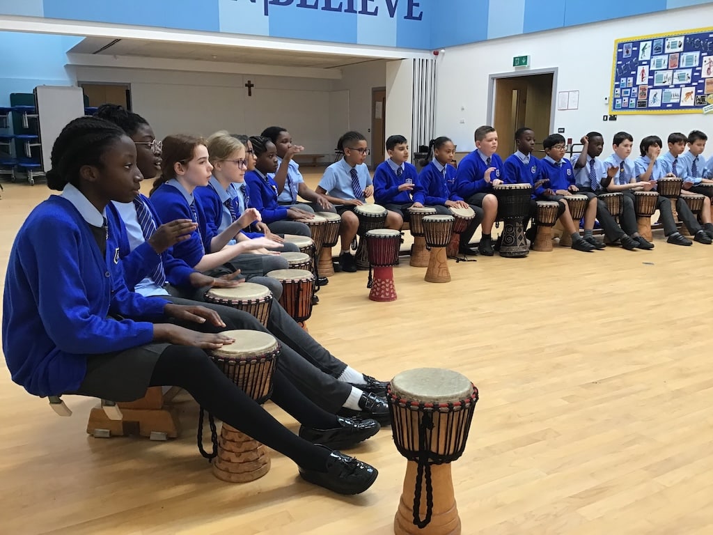 Students drumming indoors, wearing uniforms.